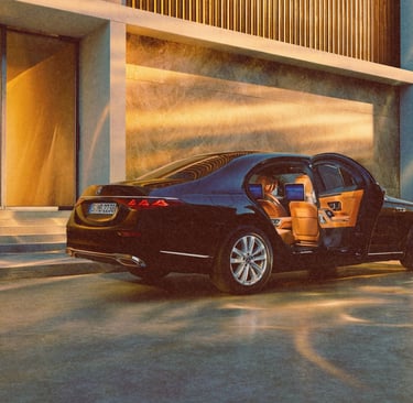 Black Mercedes-Benz S-Class luxury sedan with open rear door and tan leather interior at sunset.