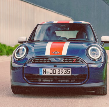 Front view of a blue Mini Cooper S with white and red racing stripes parked on a road.