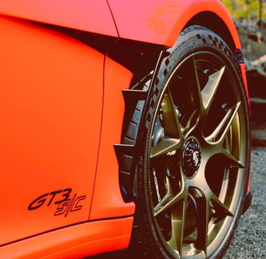 Close-up of an orange Porsche GT3 S/C fender and gold alloy wheel with high-performance tires.
