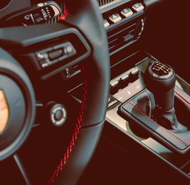 Close-up of a Porsche interior featuring a manual gear shifter and leather steering wheel with red stitching.