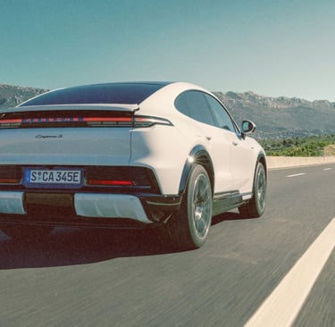 A white Porsche Cayenne S E-Hybrid Coupe driving on a highway with mountain views.