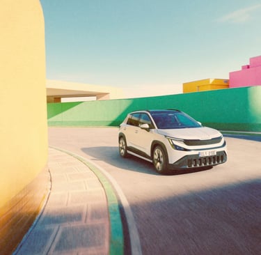 White Skoda Epiq electric SUV driving on a road surrounded by colorful pastel buildings.
