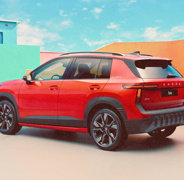 Red Skoda Epiq electric compact SUV parked in front of colorful modern architecture under a blue sky.