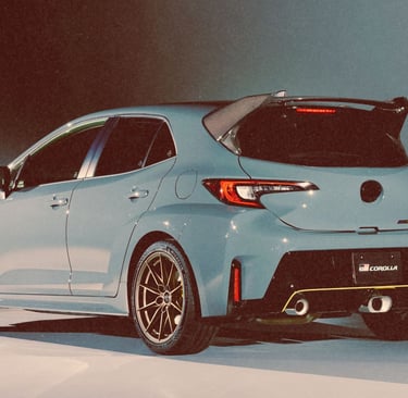 A light blue Toyota GR Corolla hatchback with a carbon fiber rear spoiler and performance alloy wheels.