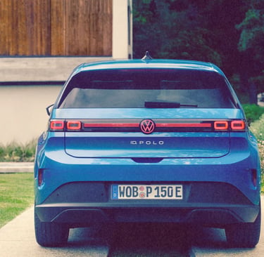 Rear view of a blue Volkswagen ID. Polo electric car parked on a driveway near a garden.