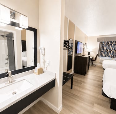 Modern hotel room with two queen beds, a vanity sink, and a flat-screen TV.