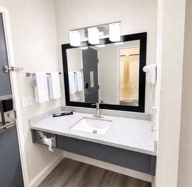 Modern hotel bathroom vanity with granite countertop, square sink, and black framed mirror.