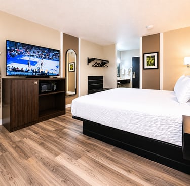 Modern hotel room with king bed, flat-screen TV, wood flooring, and ironing station.