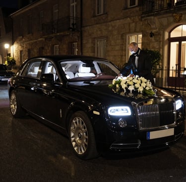 A chauffeur in a tuxedo arranges wedding flowers on a black Rolls-Royce luxury VIREMONT CHAUFFUER 