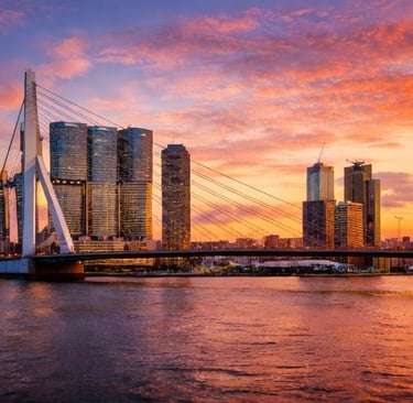 Rotterdam skyline and Erasmus Bridge at sunset with vibrant orange clouds over the Maas river.