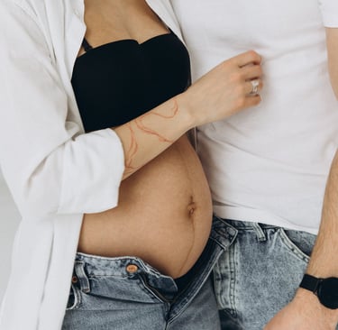 Close-up of a pregnant woman's belly with partner in a maternity photo shoot wearing denim jeans.