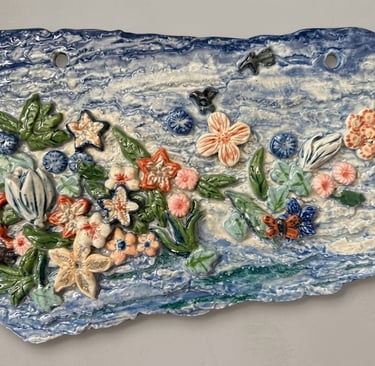 Ceramic plaque of tropical flowers floating on ocean waves, titled Tides of Aloha.