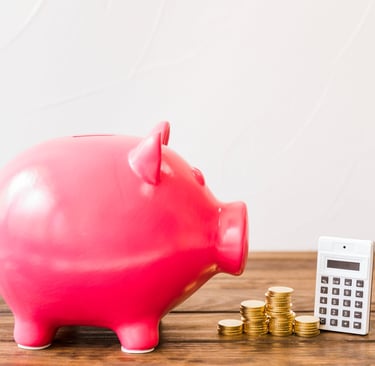 Pink piggy bank with gold coins and a calculator on a wooden table for financial planning.