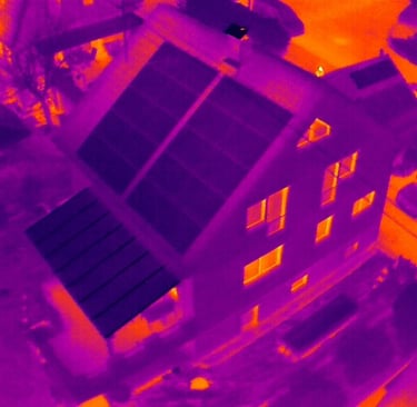 Aerial thermal imaging scan of a house showing heat loss through windows and energy-efficient solar panels.