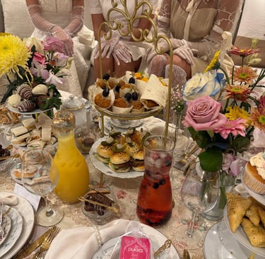 Dames met handschoentjes die aan een prachtig gedekte tafel zitten voor een high tea