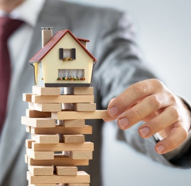 Stack of wooden blocks with a small house on top and a person's hand, symbolizing real estate invest