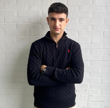 a man in a sweater and jeans standing in front of a white brick wall