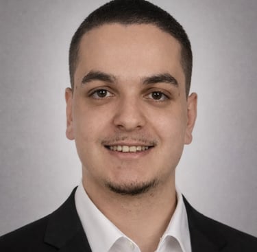 Professional headshot of a smiling young man in a black suit and white shirt.
