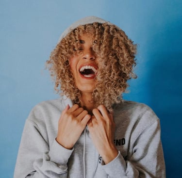 Vrouw met krullend haar in een hoodie, lachend en blij.