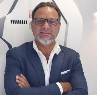 a man adnan sarfraz in a suit and glasses standing in front of a wall