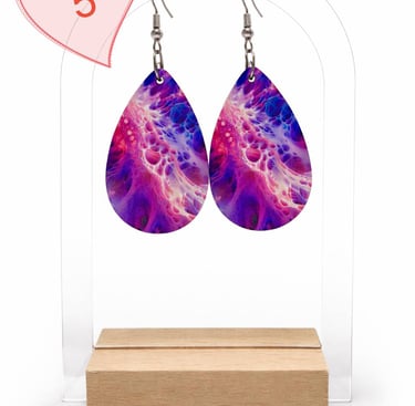 Purple and pink teardrop earrings with an abstract fluid art design on a clear display stand.