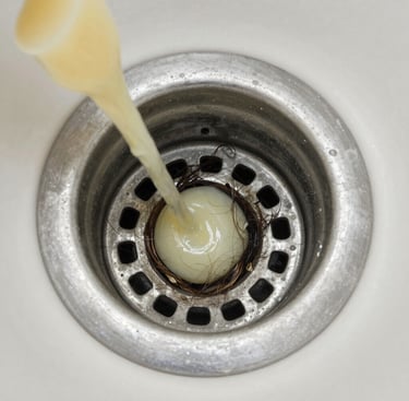 Liquid drain cleaner pouring into a clogged sink drain filled with hair and residue.