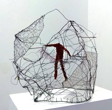 A modern wire sculpture featuring a red human figure suspended within a complex mesh cage.