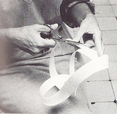 Close-up of hands using scissors to cut a strip of white paper ribbon in a black and white photo.