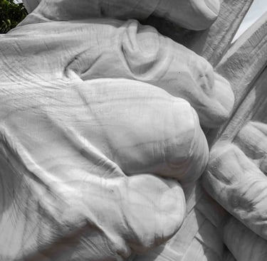 White marble sculpture of large hands weaving a mat with esparto grass on a stone pedestal in a squa