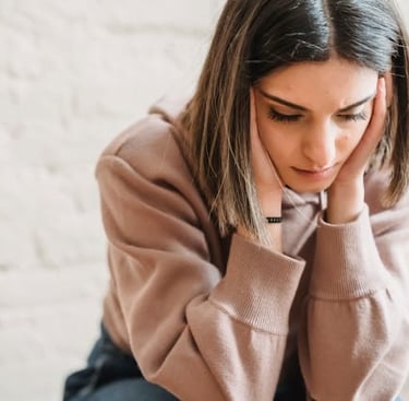 Stressed young woman in a pink hoodie holding her head in her hands, reflecting anxiety and mental fatigue.
