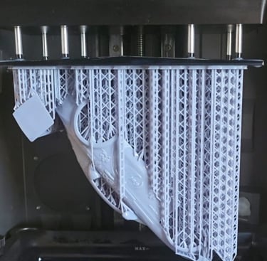 A gray resin 3D printed model with support structures hanging from a build plate inside an SLA 3D printer.