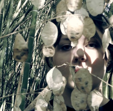 Film still from "As I Bury My Face Into My Hands" by Tina Bikic of a face partly hidden among tall plants.