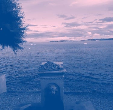 Film still from "Unfinished" by Tina Bikic of a stone fountain by the sea with mountains and boats in the distance.
