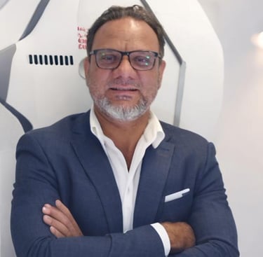 a man adnan sarfraz in a suit and glasses standing in front of a wall