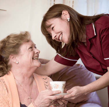 Picture of an AMG Nursing employee/nurse providing a cup of tea to a patient in her home