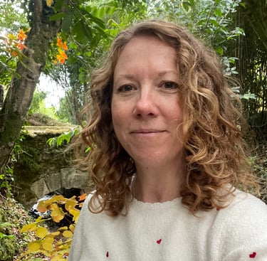 Headshot of Iona Reading standing in front of trees and a bridge