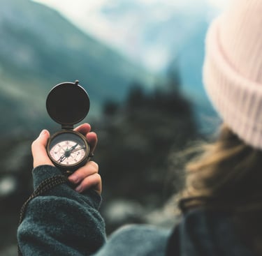 woman's hand holding compass in front of blurry nature backdrop