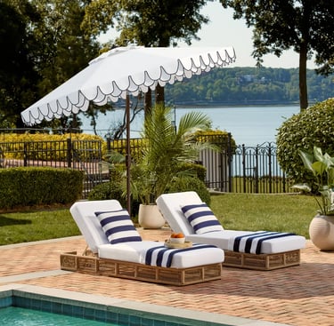 Luxury poolside lounge chairs with white cushions and a fringed patio umbrella overlooking a lake.