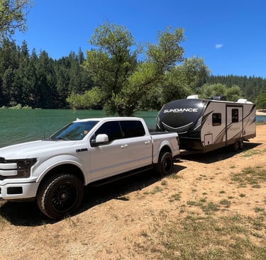 white ford f150 hooked to camping trailer in front of rollins lake