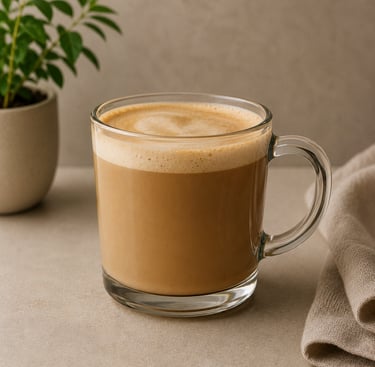 A frothy hot latte in a clear glass mug on a stone countertop with a small potted plant.