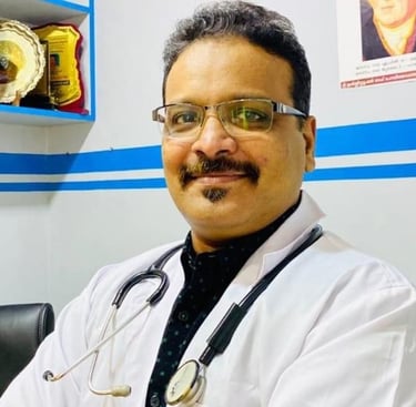 A smiling male doctor wearing a white lab coat and stethoscope in a medical clinic office setting.
