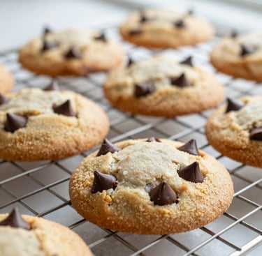 Close-up macro shot of freshly baked chocolate chip cookies on a wire cooling rack, melting chocolate chips, warm morning window light, shallow depth of field.