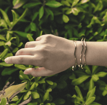 Elegantes brazaletes de oro con diseño ondulado, lucidos en una muñeca sobre un fondo de naturaleza