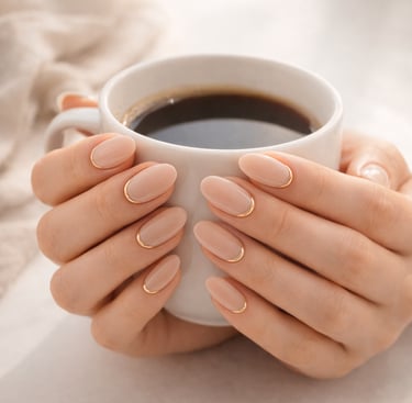 Elegant nude manicured nails with gold French tips holding a white coffee cup.