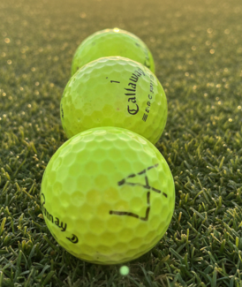 Three yellow Callaway golf balls lined up on a green grass fairway at sunset.