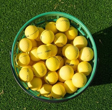A green basket filled with yellow golf balls on a lush grass turf at a driving range.
