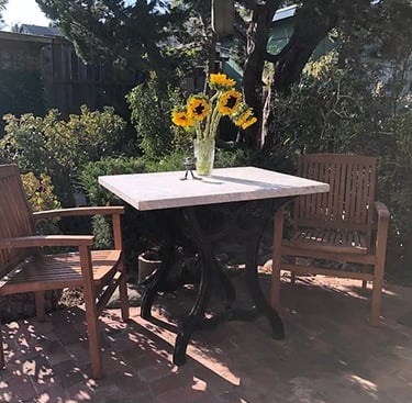 Exterior table with base made from cast iron legs from vintage paper cutter holding a white marble tabletop.