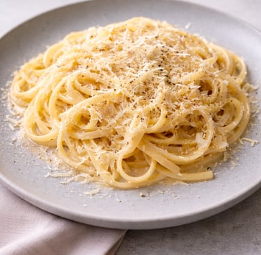 A plate of creamy Cacio e Pepe pasta topped with grated Pecorino Romano cheese and black pepper.