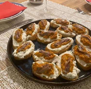 Gourmet bruschetta appetizers topped with creamy cheese, red pesto, and anchovies on a black plate.