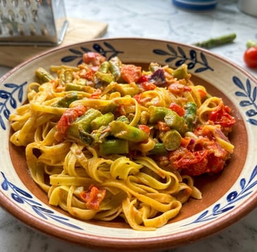 Creamy tagliatelle pasta with fresh asparagus and roasted cherry tomatoes in a ceramic bowl.